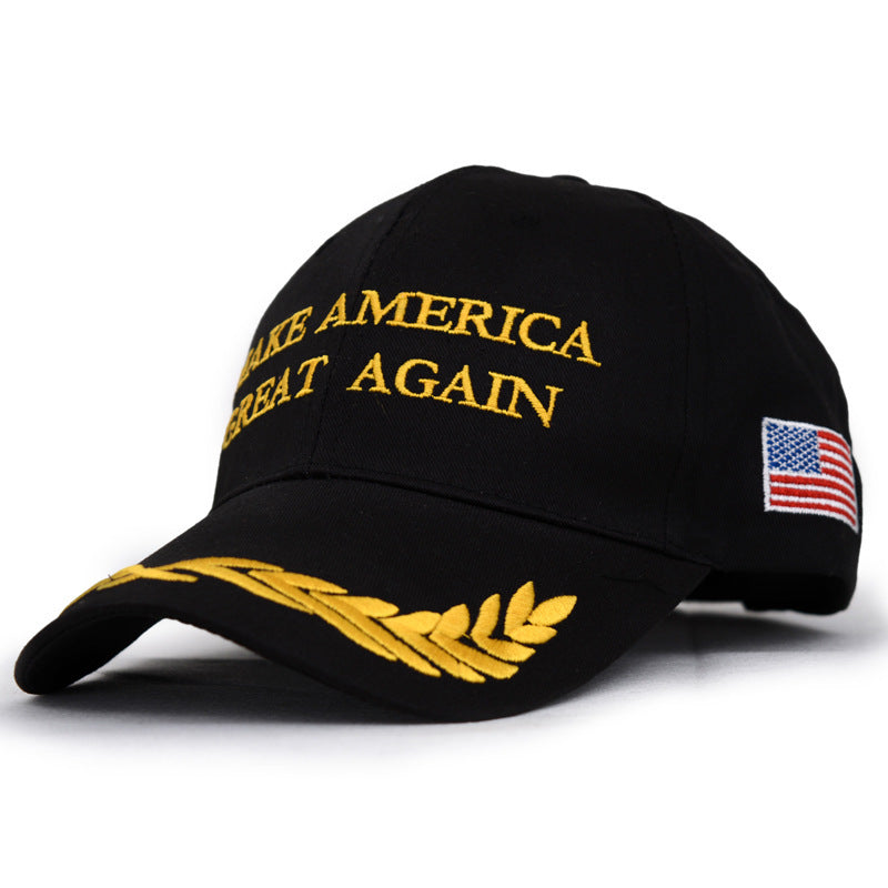 A black cap with yellow embroidery reading "Make America Great Again" on the front. The visor has a gold leaf design, and an American flag is embroidered on the side.