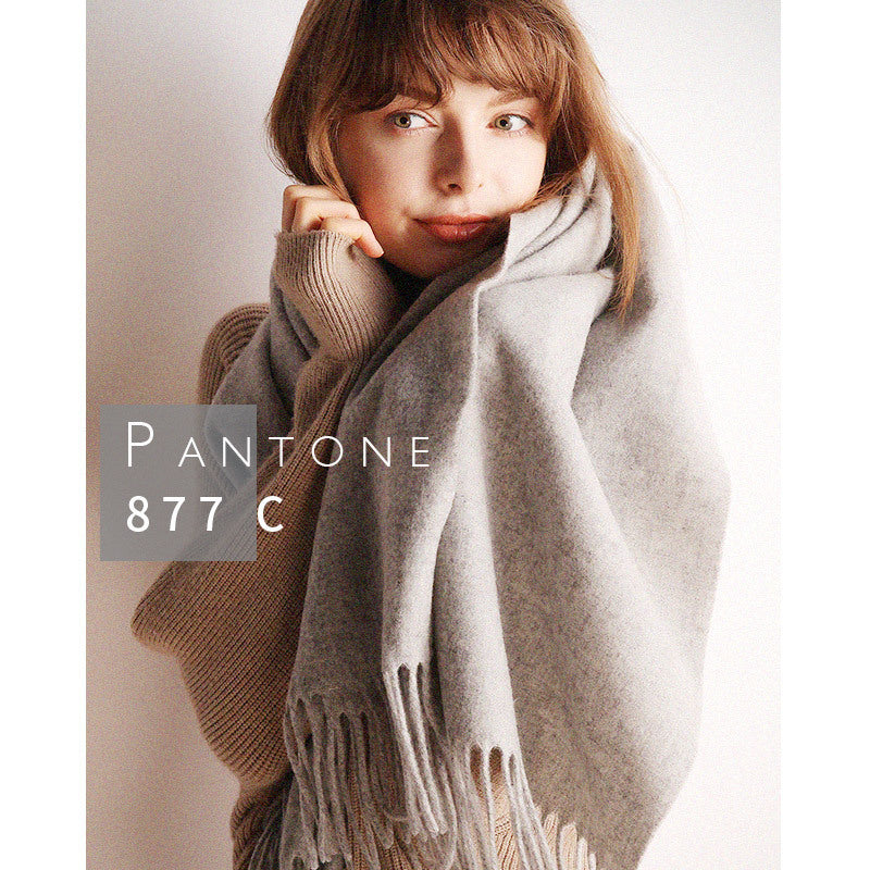 A person smiling, wrapped in a cozy gray scarf, with "Pantone 877 C" displayed on the left, symbolizing the scarf's color tone. The person wears a beige sweater, set against a soft white background.