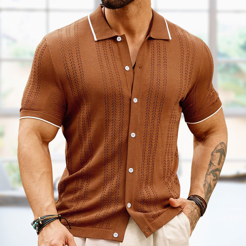 A person in a Men's Short Sleeve Knitted Polo Shirt with a textured pattern and white trim stands indoors. The classic style is accentuated by their tattooed left arm and multiple bracelets, while soft daylight filters in through a large window in the background.