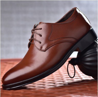 A pair of CJ'S Men's Sleek Black Pointed Toe Shoes is displayed on a textured brown surface. These shoes feature black laces, a black rubber sole, and a slight heel, offering both style and comfort. Their breathable interior ensures all-day wearability, while they sit with the toes slightly elevated, perfect for casual fashion.