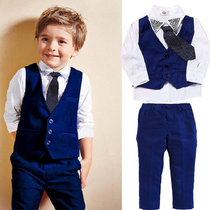 A young boy wearing The Smart Gift Shop's Boys' Formal 3-Piece Suit, featuring a high-quality vest and pants in royal blue, paired with a white shirt and polka-dotted tie, smiles against a light background. Beside him is a close-up of this elegant suit laid flat, highlighting the sophistication of boys' clothing.