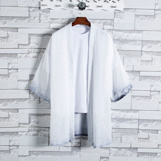 A stylish Men's Lightweight Gradient Kimono Cardigan, featuring a trendy loose fit and grey ombre edges, hangs on a decorative white hanger against a textured white brick wall. A plain white T-shirt worn underneath highlights its versatile styling options, creating a chic layered look.