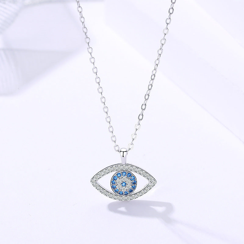 The CJ'S Blue Evil Eye Necklace with Sparkling Crystal Accents features a delicate protection chain that holds a blue circular center accented with sparkling crystals and bordered by a shimmering silver outline encrusted with stones.