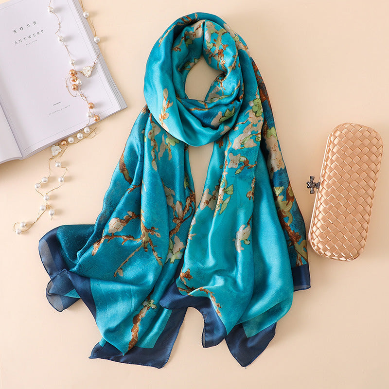 A CJ'S Summer Sunscreen Shawl Scarf featuring a luxurious floral pattern is elegantly draped on a beige surface. It is accompanied by an open book with a string of pearls, and a beige woven clutch purse with a metal clasp placed nearby.