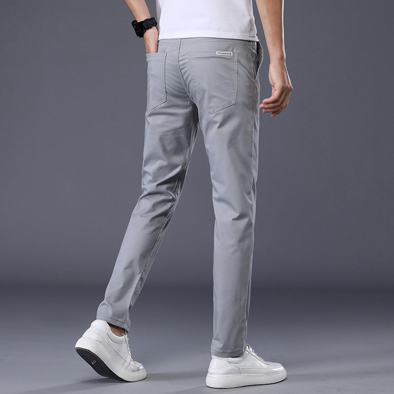 A person models the Men's Slim-Fit Stretch Casual Pants - Comfortable and Stylish, paired with white sneakers, exuding versatile style and all-day comfort against a plain backdrop. Facing away from the camera, they highlight a white shirt and a black wristwatch.