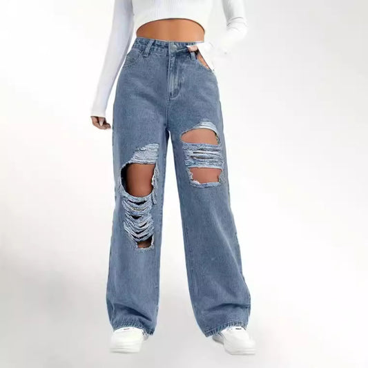 A person is wearing Zendrop's European And American Fashion Ripped High Waist Jeans in light blue, featuring large holes and frayed edges on both thighs. They are also sporting a long-sleeved white crop top and white sneakers, giving off a retro style vibe against a plain, light-colored background.