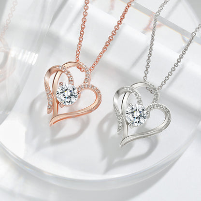 Two elegant Double Heart Crystal Pendant Necklaces by CJ'S are displayed, one in rose gold and the other in silver. Each piece features intertwined hearts adorned with sparkling crystals and a central round-cut diamond-like gem, all on delicate chains that exude sophistication and charm.