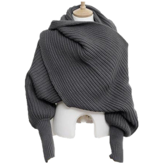 A grey, chunky knit CJ'S sweater-scaf draped on a mannequin. The woolen piece appears to have a soft, textured weave and features long sleeves and a cozy, oversized fit, lending it a casual and comfortable look.
