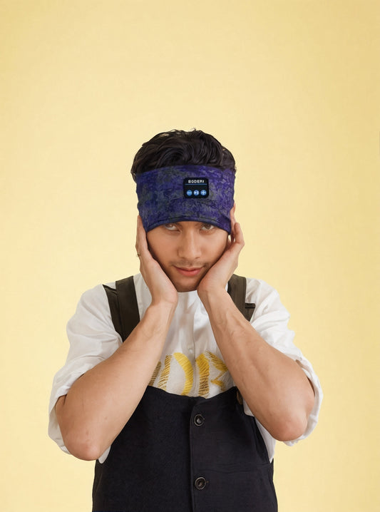 A person wearing the CJ'S Wireless Bluetooth Headband with Built-in Speakers for Sleep and Workouts holds both sides of their head with their hands. Dressed in a white shirt with a black vest, they gaze forward. The background is a solid yellow color, suggesting they are enjoying a comfortable music experience.