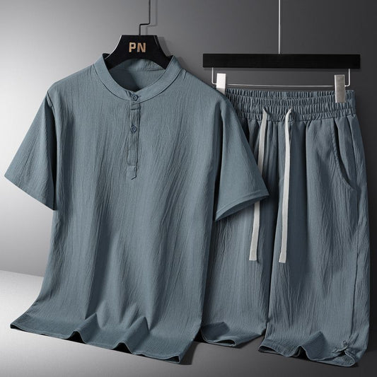 Zendrop's Men's National Style Cotton And Linen Casual Shorts Short Sleeve Two-piece Set features a mandarin collar button-up shirt with two buttons and drawstring shorts. Made from light blue-gray polyester fabric with a textured finish, the shirt sports a short-sleeve design while the shorts have an elastic waistband with white drawstrings, available in Asian sizes.