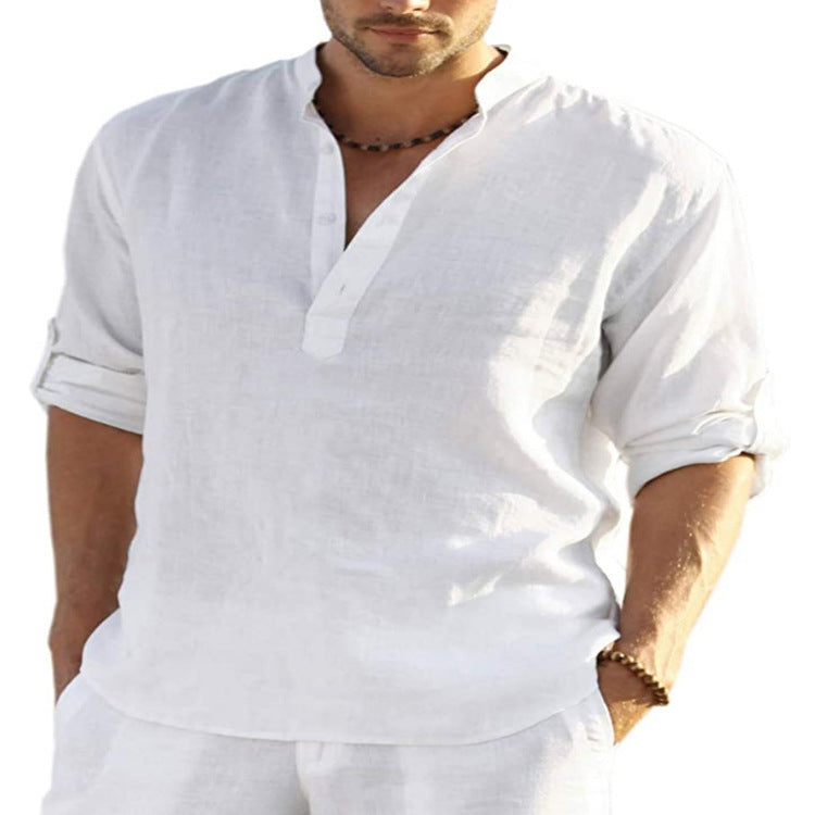 A man showcasing a relaxed style is wearing the Men's Casual Cotton Linen Long Sleeve Shirt, made from breathable fabric. The shirt has rolled-up sleeves and a partially buttoned-up design, paired with his hands tucked into the pockets of matching white pants and accessorized with a necklace.