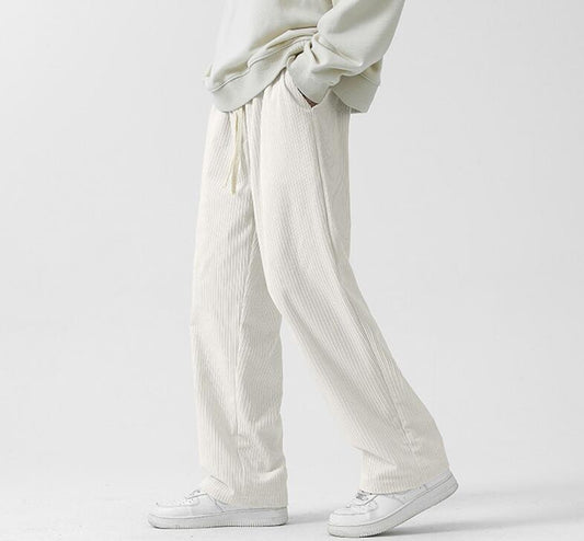 A person is seen wearing a pair of Men's Wide-Leg Corduroy Pants with Drawstring Waist - Casual Comfort, paired with a light-colored sweater and white sneakers. They stand against a plain white background, while the photo highlights their lower half to emphasize the comfortable casual wear ensemble.