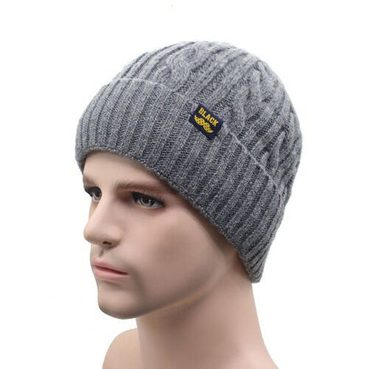 A mannequin head showcases the CJ'S Cosy Winter Knit Beanie, a soft and warm stretchable cold weather hat knitted in gray. It features a small label that reads "BLACK" along with a winged emblem, all set against a plain white background.