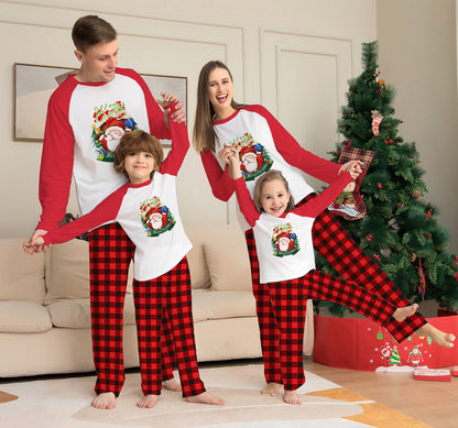 A joyful family of four in matching "Family Matching Christmas Pyjamas - Santa & Plaid Holiday Set" stands in the cozy living room by the decorated Christmas tree. Dressed in soft cotton home wear, their red and white tops with festive designs and red plaid pants beautifully highlight the warm parent-child bond as they smile and hold hands.