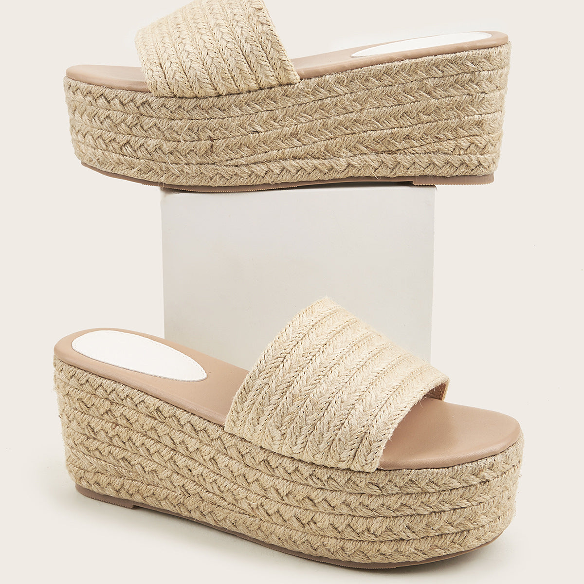 A pair of Women's Summer Wear Everyday Joker Elevator Shoes from Zendrop is displayed, one propped on a white block and the other standing on the surface. The sandals resemble stylish slippers, featuring a thick rubber sole with a rope-like texture and a wide strap over the toes, creating a casual and summery look.