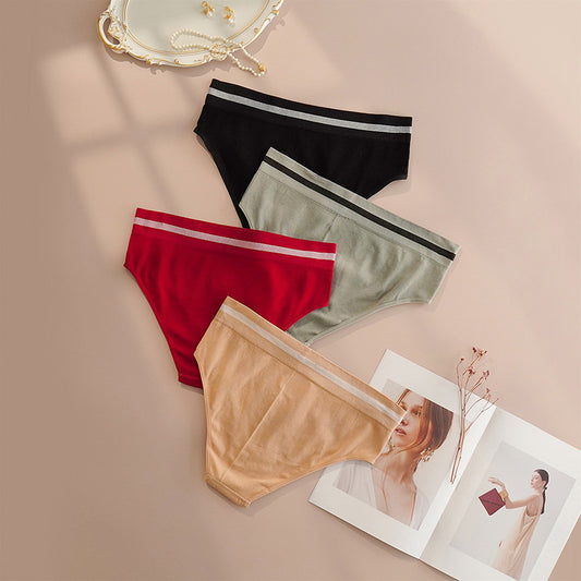 Four pairs from the Women's Comfortable Everyday Panty Set, available in black, gray, red, and beige, are displayed on a surface. Nearby, an open magazine shows a woman in a white outfit beside a decorative mirror on the left. Crafted from soft and breathable fabric, these panties offer a seamless fit for no visible panty lines under clothing.