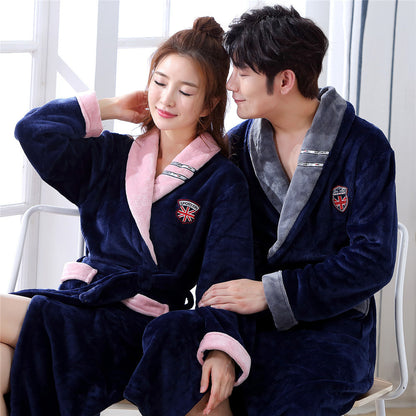 A couple in matching blue robes sits on a white bench. The woman's robe, with its pink trim, beautifully complements the man's gray-trimmed robe. They sit closely, smiling warmly at each other in the natural light from a nearby window—an ideal setting to showcase the Elegant Winter Flannel Robe for Couples, perfect for keeping cozy and comfortable during winter nights.