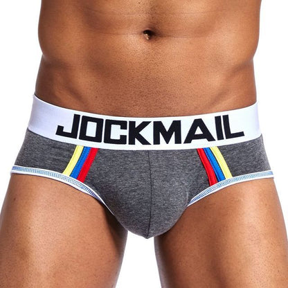 The Men Underwear Briefs U Convex Big Pouch Jockstrap by Jockmail feature a high waist with a prominent white waistband displaying the brand name. The gray design is enhanced by striking red, yellow, and blue stripes on the front.