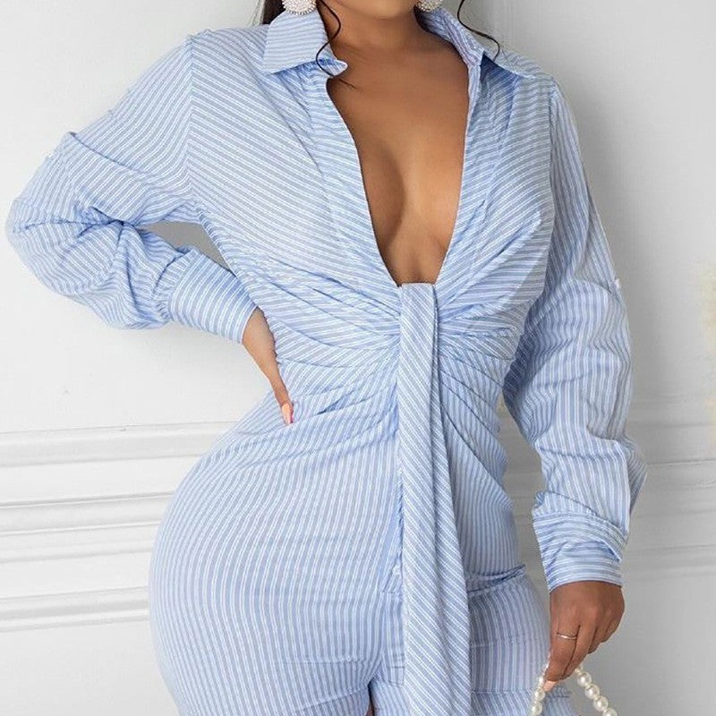 A person wearing the Deep V Strap Tight One-piece Shorts, styled in light blue and white stripes and made from Polyester Fibre, stands against a white wall. This outfit showcases long sleeves, a deep V-neckline, and a knotted waist design that enhances the accessorized look.